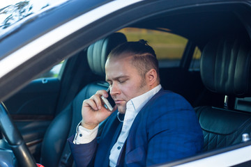 a serious businessman in tha jacket standing sitting in the car holding mobile phone