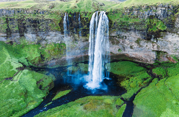 Iceland. Fantastic view of Seljalandsfoss waterfall. Water flow at covered with green grass cliff background. Iconic travel destination. Green color in Northern nature. Landscape photography.