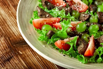 warm salad with chicken liver and grapes on a wooden table