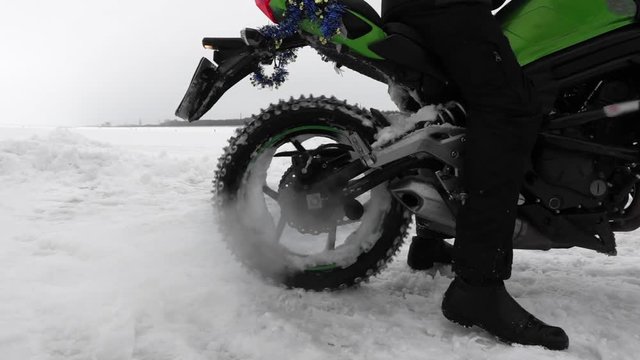 Motorcycle rider on snowy motocross track. Motorcycle wheel slipping on snow stucking in snowdrift, closeup. Wheel turns in the snow in slow motion. Motocross winter season race.