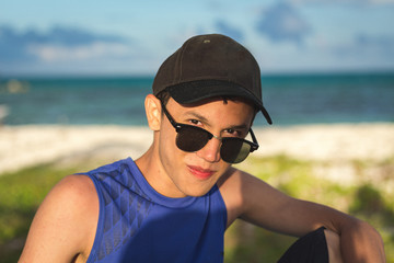 hombre joven con gafas y gorra en la playa mirando 