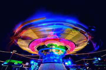 Bright colorful carosuell in neon colors in motion at a fun fair during evening. - obrazy, fototapety, plakaty