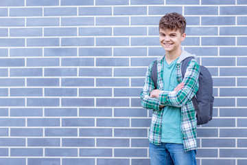 Schoolchild go to school with backpack. Smiling cute child - teen boy with bag against a brick wall outdoors. Childhood and Back to school concept.