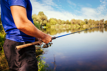 Young man fishing on river at sunset. Closeup of fiserman holding rod. Fishing equipment. Spinning