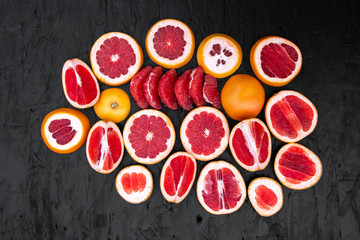 Ripe juicy cut red grapefruit slices on black wood background closeup