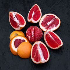 Ripe juicy cut red grapefruit slices on black wood background closeup