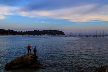 Fototapeta na wymiar View of the beach, two bathers on a rock, bay of Beaulieu sur Mer, Saint Jean Cap Ferrat at sunset