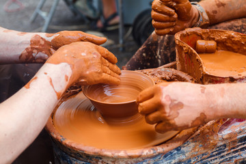 Close up pottery. Adult potter muddy hands guiding child hands to help with clay on a wheel. Child trying to make a simple clay pot or plate