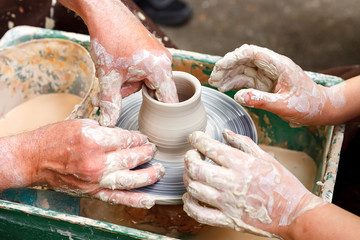 Close up pottery. Adult potter muddy hands guiding child hands to help with clay on a wheel