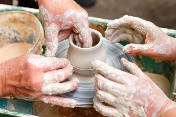 Close up pottery. Adult potter muddy hands guiding child hands to help with clay on a wheel
