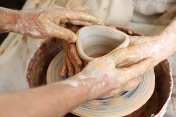 Close up pottery. Adult potter muddy hands guiding students hands to help with clay on a wheel