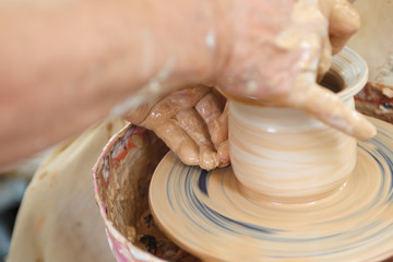 Close up pottery. Selective focus. Adult potter muddy hands guiding students hands to help with clay on a wheel