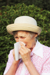 An elderly woman in the park is unwell, she is allergic. Spring-summer period. Flow snivel, tears and senior sneezes.