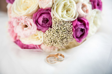 Wedding rings and a bouquet on a white surface, there is space to insert text