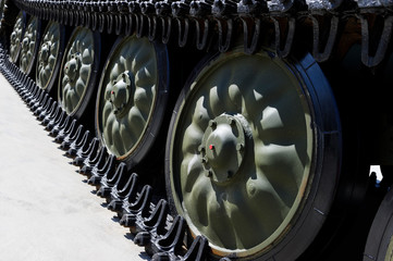 Tank tracks and steel wheels of heavy armored vehicle with green bodywork, military industry, modern army equipment, selective focus 
