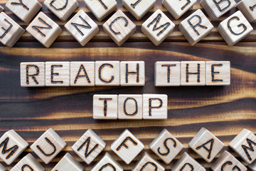 reach the top - phrase from wooden blocks with letters, achieve success or strike oil concept, random letters around, top view on wooden background