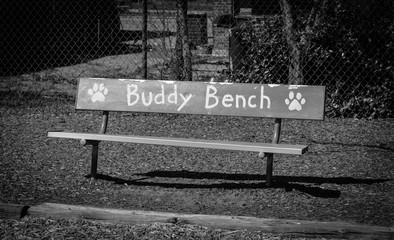 A bench at a elementary school playground for a lonely child to sit on to show they need a friend or a buddy - Black and white image - social issue 