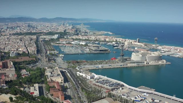 Aerial shot of large Barcelona port with maritime station for ferries, yacht harbors, fishing port, car cable tower and landing areas for ships. Drone shot of city buildings and sea coast of Barcelona