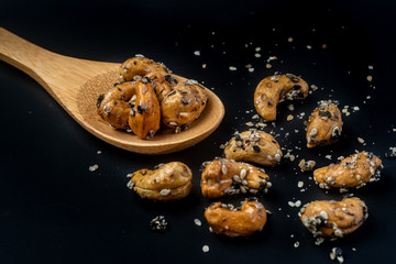 Sesame Coated Cashew Nuts on wooden spoon. Isolated on black background