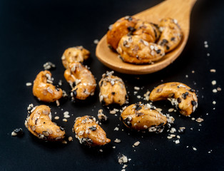 Sesame Coated Cashew Nuts on wooden spoon. Isolated on black background