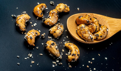 Sesame Coated Cashew Nuts on wooden spoon. Isolated on black background
