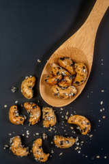 Sesame Coated Cashew Nuts on wooden spoon. Isolated on black background