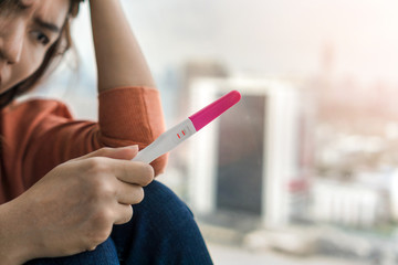 Unhappy young asian woman holding pregnancy test showing a positive result, Wellness and healthy concept, Abortion problem, Selective focus.