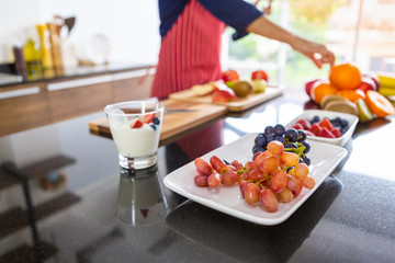 Closeup bunch of grapes on white plates and assorted fruits yogurt on black wooden table in kitchen room