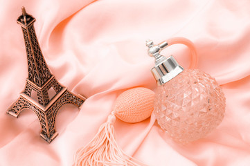 Pure essence perfumes, fragrance of France and romantic mood in Paris concept theme with a vintage bottle of french perfume on pink silky satin or silk next to miniature replica of the Eiffel Tower