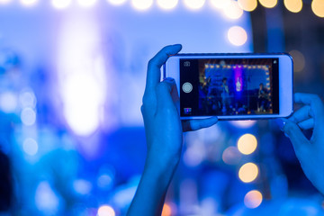 Fototapeta na wymiar Silhouette of guest hands using smartphone as camera to take pictures and videos of wedding ceremony on stage with bokeh light. Audience taking photo of concert or events by mobile phone at night.