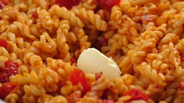 A tablespoon size piece of unsalted butter melting  and reducing its size on a pan with fusilli pasta and tomato sauce