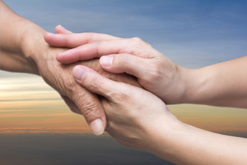 Caregiver, carer hand holding elder hand in hospice care with sky sunset background. Euthanasia ...
