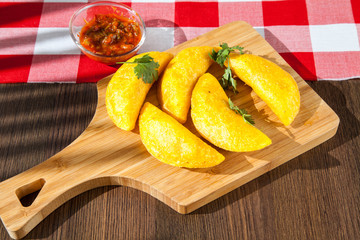 Colombian empanada with spicy sauce on wooden background