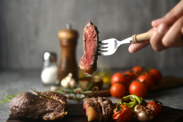 Steak pieces on a fork holding by hand, surrounded by flavoring ingredients, horizontal image.