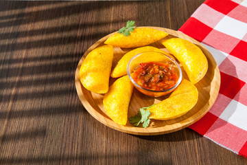 Colombian empanada with spicy sauce on wooden background