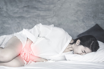 Asian woman laying down on bed hand holding her crotch suffering from pain,itchy concept background 