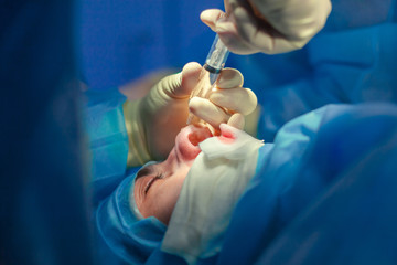 Surgeon and his assistant performing cosmetic surgery on nose in hospital operating room. Nose reshaping, augmentation. Rhinoplasty.