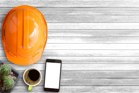 Orange Safety Helmet,cactus And Cup Of Coffee On White Wood Table Background In Office Desk Or Workplace.