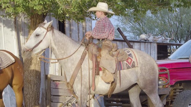 Young cowboy rancher kid adjusting saddle seating before country ride in Texas 4k