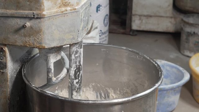Baker tipping water into the big mix container for the bread dough
