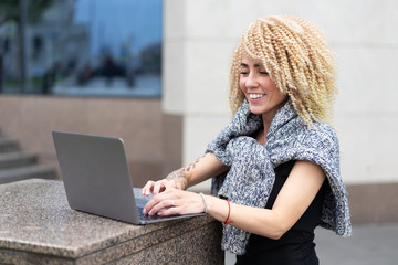 Hipster girl with afro hairdo in jacket working outside on laptop. Office in open air. Freelance on...