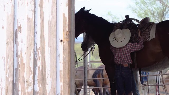 Young Ranchers Adjusting Saddle On Horse In Stables.