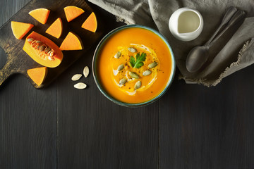 Pumpkin cream soup in a bowl with pumpkin seeds, parsley, cream and fresh orange butternut squash slices on wooden table. Traditional fall, Thanksgiving meal. Healthy organic vegetarian food. Top view