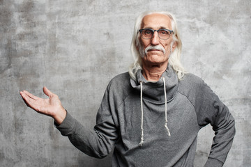 Gray haired Caucasian grandfather with glasses pretending to be holding something in hands, advertising your product on gray background isolated