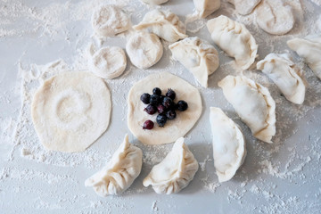 On the table, sprinkled with flour, a circle of dough is rolled out with a filling in the middle, irgi berries.Cutting test. Cooking dumplings or ravioli with fresh berries concept.