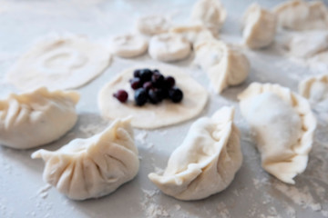 Obraz na płótnie Canvas Sculpted dumplings with Irga, raw dough. Stages of preparation of sweet flour boiled dishes. White table with flour and roll the dough.