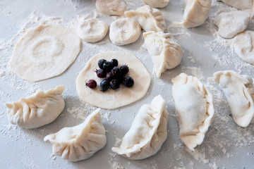 Sculpted dumplings with Irga, raw dough. Stages of preparation of sweet flour boiled dishes. White table with flour and roll the dough.