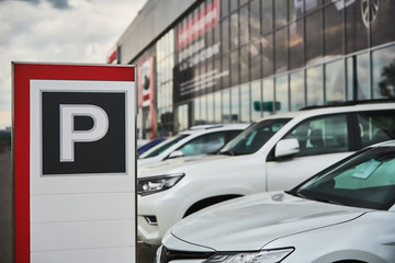 Fototapeta premium A parking sign at a car dealership close-up and the cars behind it.
