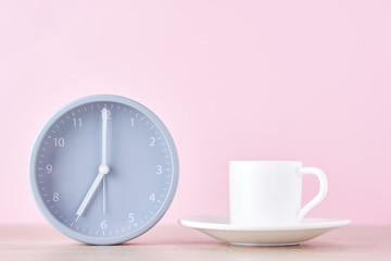 Classic gray alarm clock and white coffee cup on a pink background