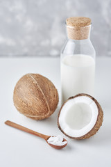 Coconut milk in glass bottle and fresh coconuts with half on a gray background